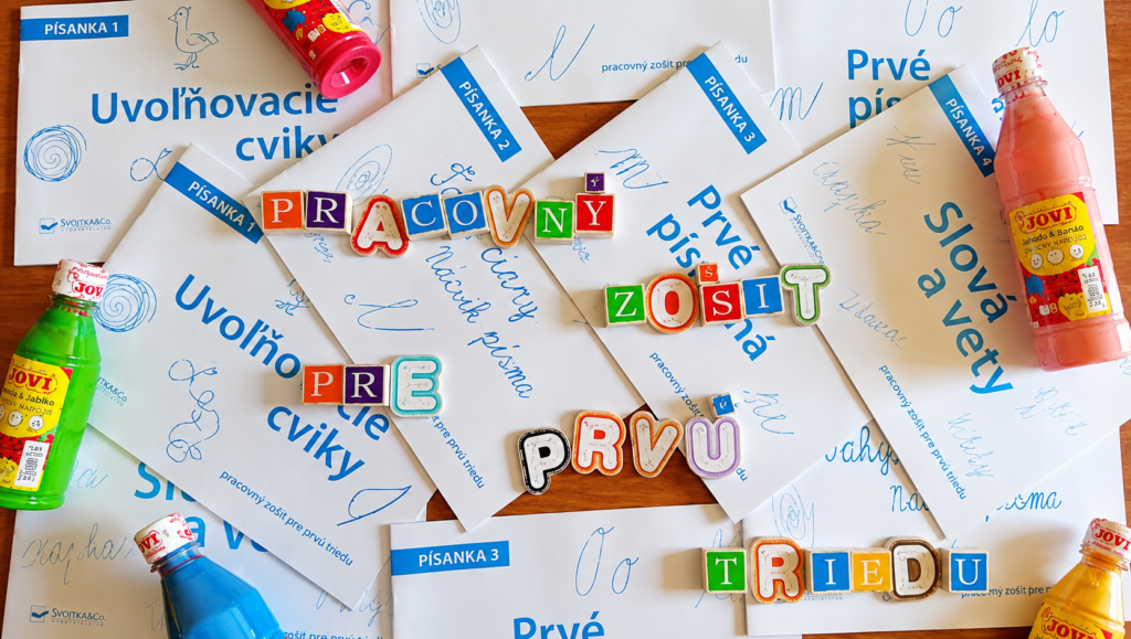 Pracovné zošity Písanky pre prvákov s farebnými písmenami skladajúcimi nápis „Pracovný zošit pre prvú triedu“ a školskými pomôckami.